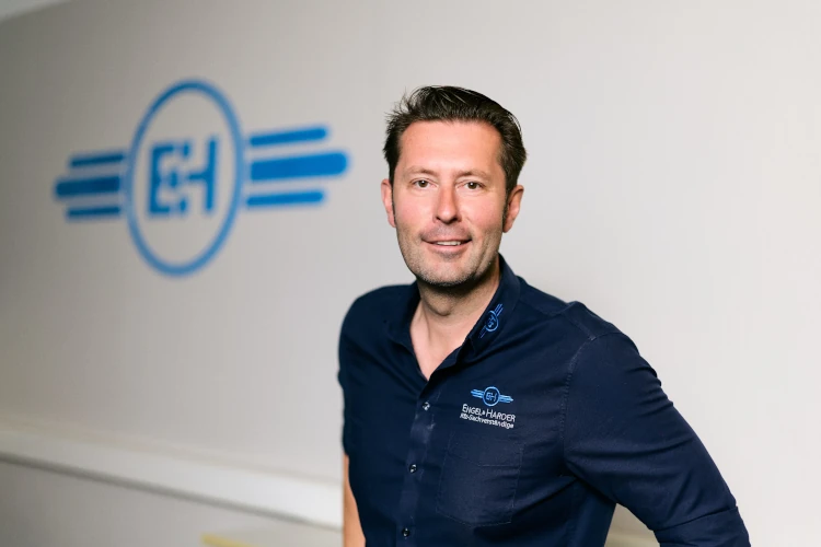 Ein Mann steht vor einer Wand mit dem Logo einer Elektroinstallationsfirma im Hintergrund.